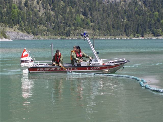 Das Boot der Feuerwehr Reutte zieht die Ölsperre über den Plansee